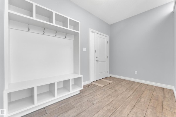 Mudroom with white built-in storage, bench, hooks, light wood floor, and a white door. - 4359 126 Av Nw, Edmonton