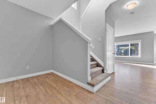 Interior hallway with a carpeted staircase, light gray walls, and light wood flooring. - 4359 126 Av Nw, Edmonton