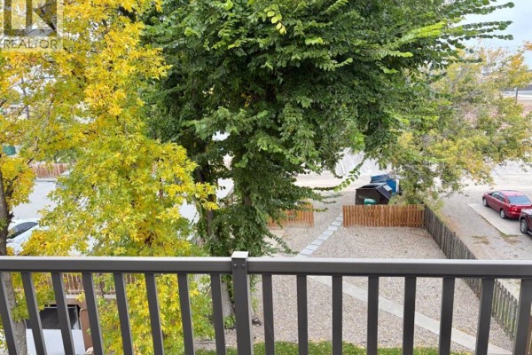 Balcony with concrete floor, grey railing, and view of trees and parking. - 436, 1237 4 Avenue S, Lethbridge