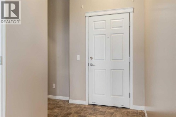 Interior view of an apartment entrance with a white door and beige walls. - 436, 1727 54 Street Se, Calgary