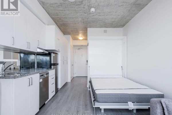 Studio apartment kitchenette with white cabinets, stainless steel appliances, and fold-down bed visible. - 436 - 1900 Simcoe Street N, Oshawa