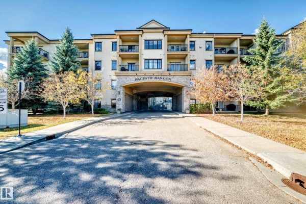 Exterior view of Magrath Mansion apartment building with a covered entryway and surrounding trees. - #436 160 Magrath Rd Nw, Edmonton