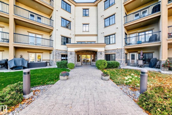 Entrance to the Magrath Mansion building with a stone facade, glass doors, and paved walkway. - #436 160 Magrath Rd Nw, Edmonton