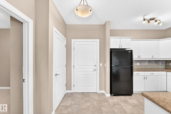 View of the apartment's entryway with a white door, beige walls, and access to the kitchen. - #436 160 Magrath Rd Nw, Edmonton