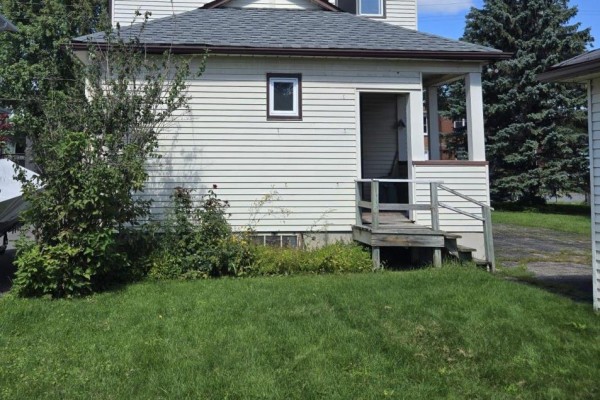 Side exterior view of the house with a small covered porch and stairs leading down to a grassy yard. - 436 Fourth Street E, Cornwall