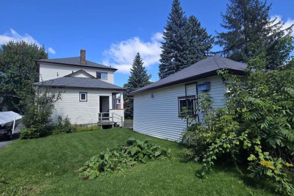 Rear exterior view showing the back of the house and a detached garage with trees and greenery. - 436 Fourth Street E, Cornwall
