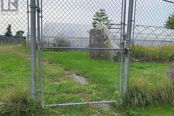 Chain-link gate with grassy area and distant structures - 43621 Highway 3, Wainfleet