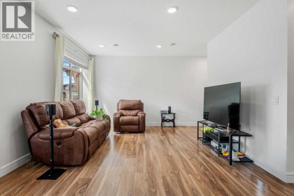 Living room with brown leather recliners, a large TV, and wooden floors. - 4367 Seton Drive Se, Calgary
