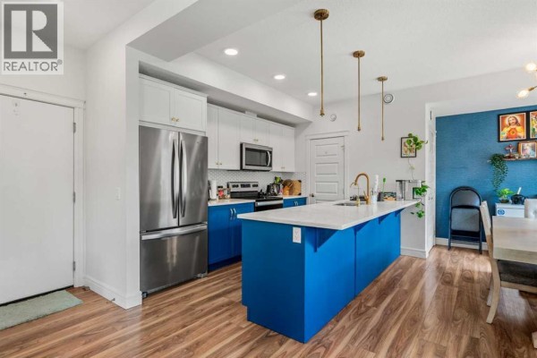 Kitchen with white and blue cabinets, stainless steel appliances, and a central island. - 4367 Seton Drive Se, Calgary