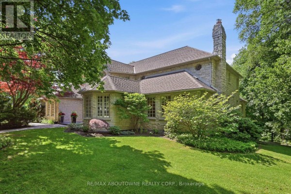 Side view of a stone house with a large stone chimney and multiple windows. - 437 Cairncroft Road, Oakville