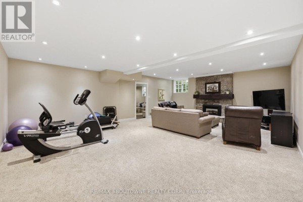 Finished basement with stone fireplace, seating, TV, and exercise equipment - 437 Cairncroft Road Oakville