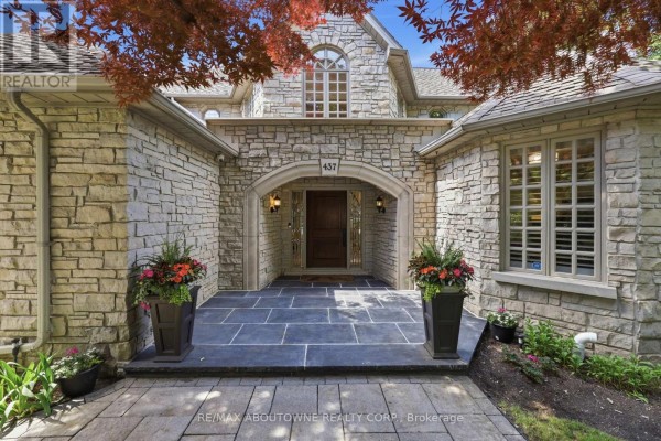 Front entrance with a stone facade, arched doorway, and two potted plants. - 437 Cairncroft Road, Oakville