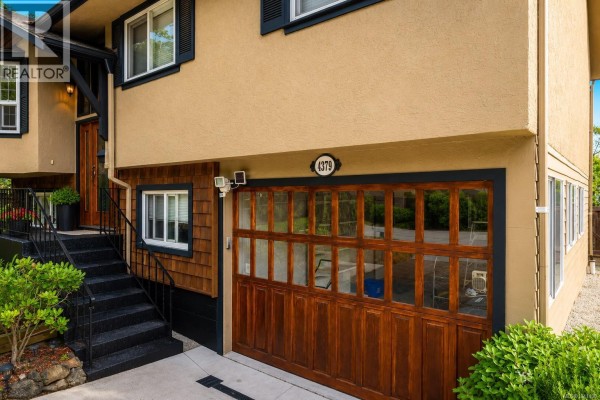 Close-up of the wooden garage door with glass panels and the house exterior with a numbered address plate. - 4379 Shelbourne St, Saanich