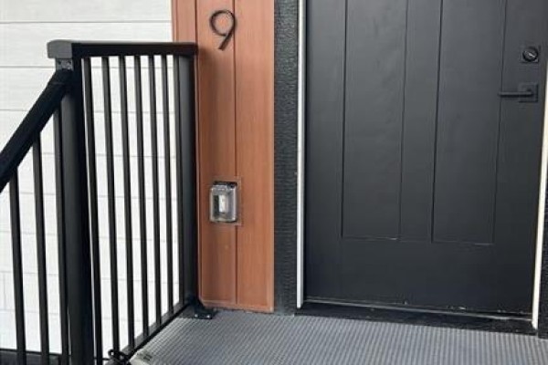 Close-up of the front door with black finish, wood trim, and metal railing. - 439 Arlington Drive Se, Calgary