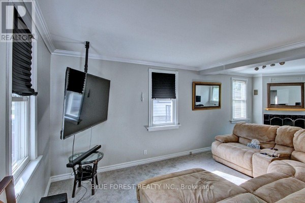 Living room with a beige sectional sofa, television, mirrors, and a fireplace surround. - 439 Beatrice Street, London East