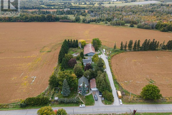 Aerial view of a farm property with several houses, a barn, and mature trees surrounded by farmland. - 4392 Solina Road, Clarington