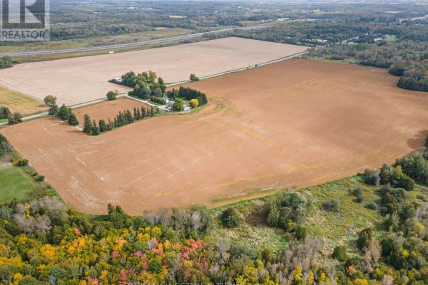 Aerial view of the farmstead and large brown fields bordered by trees and a highway in the distance. - 4392 Solina Road, Clarington