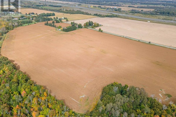 Aerial view of cultivated brown fields with scattered trees and a farmstead visible in the distance. - 4392 Solina Road, Clarington