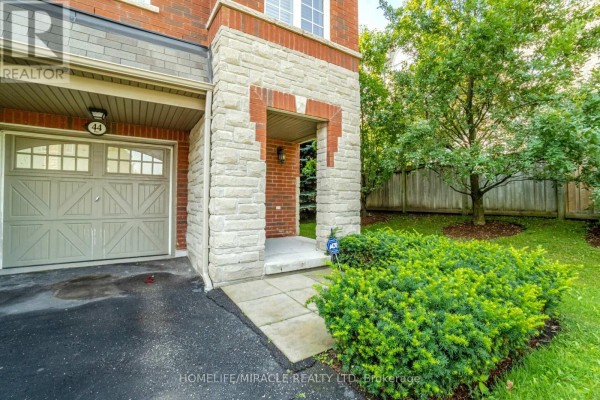Close-up of townhouse entrance with stone surround, garage door, and manicured shrubs. - 44 - 1701 Finch Avenue, Pickering