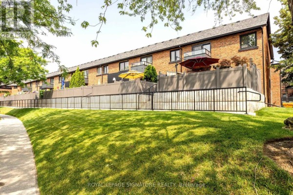 Rear view of brick townhouses with balconies, fences, and green lawn. - 44 - 51 Broadfield Drive, Toronto