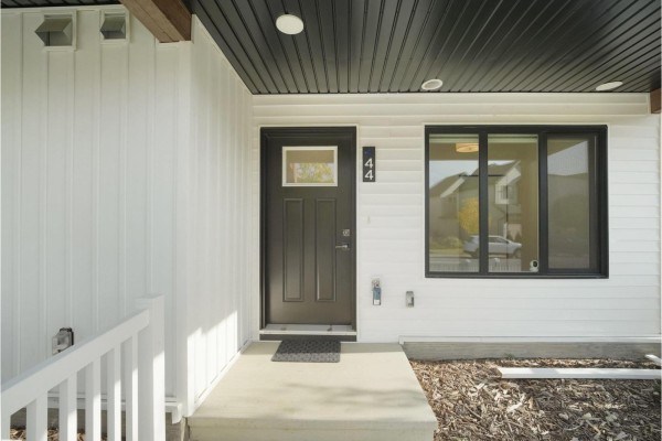 Front entrance of a townhouse with a dark gray door, white siding, and a large window. - #44 1025 Secord Promenade Pm Nw, Edmonton