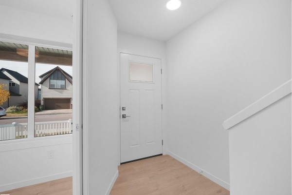 Interior view of a townhouse entryway with a white door, light wood floors, and a staircase. - #44 1025 Secord Promenade Pm Nw, Edmonton