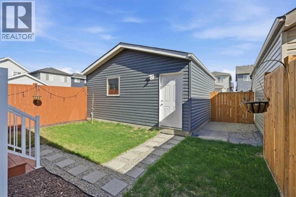 Backyard with a detached garage, green grass, gravel area, and wooden fence. - 44 Amblefield Avenue Nw, Calgary