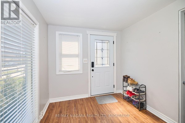 Interior entryway with wood-look flooring, white door, shoe rack, and window with blinds. - 44 Churchill Street, St  Catharines
