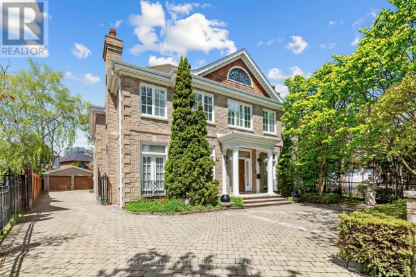 Large stone house with a paved driveway and mature trees in the front yard. - 44 Cotswold Crescent, Toronto