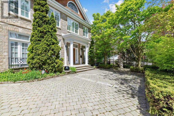 Front exterior of a large stone home with a paved driveway and landscaping. - 44 Cotswold Crescent, Toronto