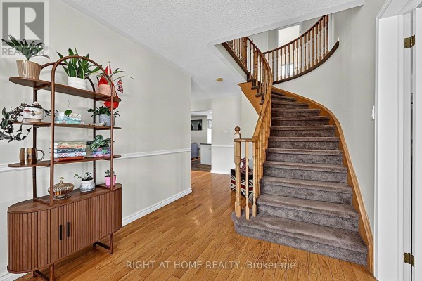 Entrance hall with a curved wooden staircase and a mid-century modern shelving unit. - 44 Edenbridge Drive, Essa