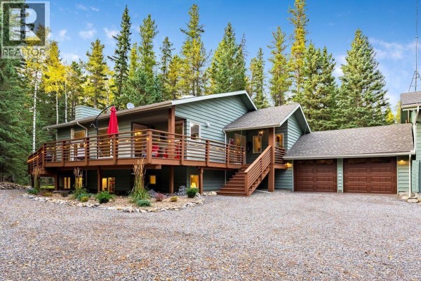 Front exterior of a green house with a wrap-around wooden deck and double garage doors. - 44 Elk Valley Grove, Rural Rocky View County