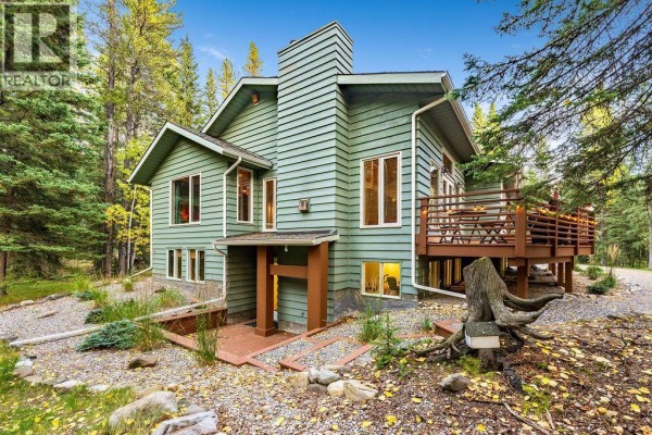 Side exterior of the green house with a brick pathway, wooden deck, and large chimney. - 44 Elk Valley Grove, Rural Rocky View County