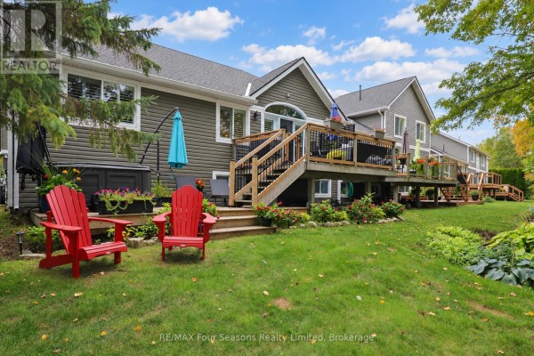 Rear view of the house with a large wooden deck overlooking a green lawn and mature trees. - 44 Green Briar Drive, Collingwood