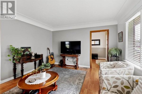Living room featuring a television, wooden flooring, and patterned armchairs. - 44 Mccrea St, Sault Ste  Marie
