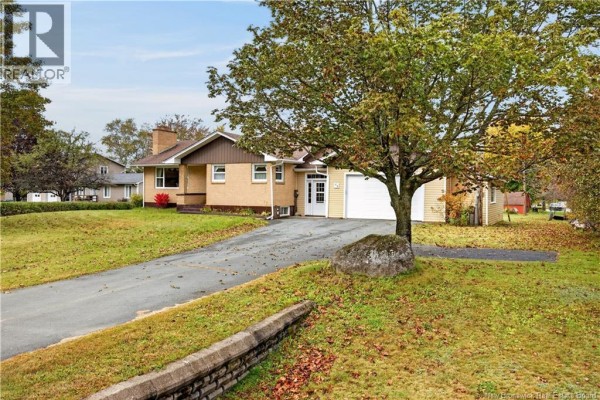 View of the house from the driveway, featuring a large tree in the foreground and the attached garage. - 44 Nelson Street, Miramichi