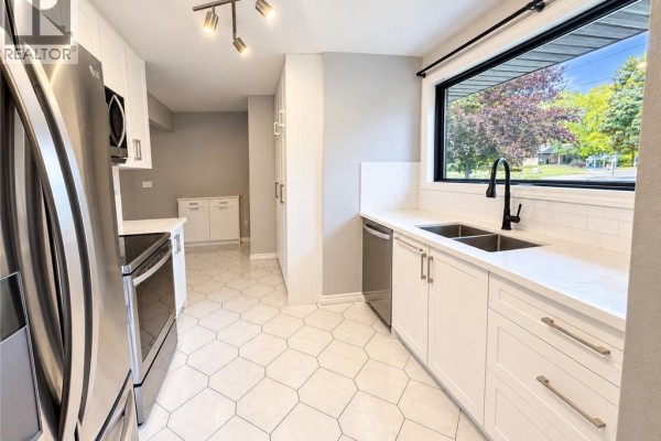 White kitchen with stainless steel appliances and large window above sink. - 44 Patterson Avenue Unit# A, Brantford