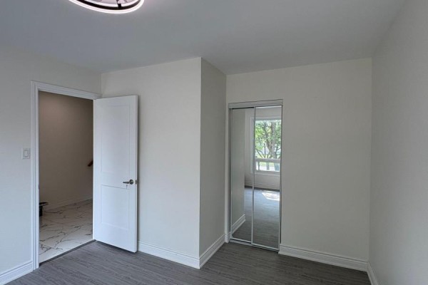 Bedroom with gray flooring, white walls, a mirrored closet, and an open doorway to a hallway. - 44 Sylvia Street, Barrie