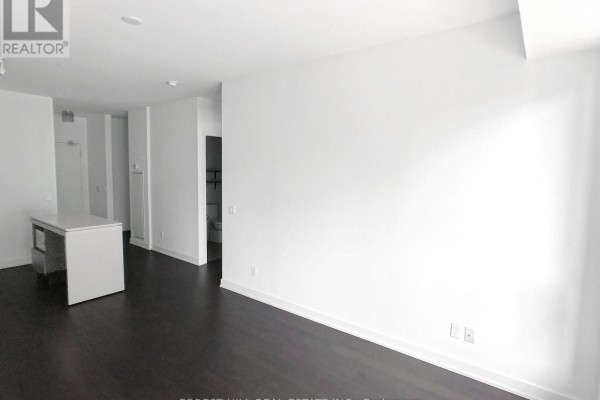Empty living space with dark hardwood floors, white walls, and an entryway. - 440 - 1030 King Street W, Toronto