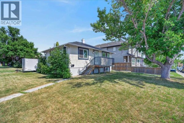 View of a single-family house with light stucco exterior, deck, and large tree. - 440 53 Avenue Sw, Calgary