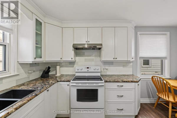 Close-up of a white stove and range hood in a kitchen with white subway tile backsplash. - 440 Howden Street, Peterborough
