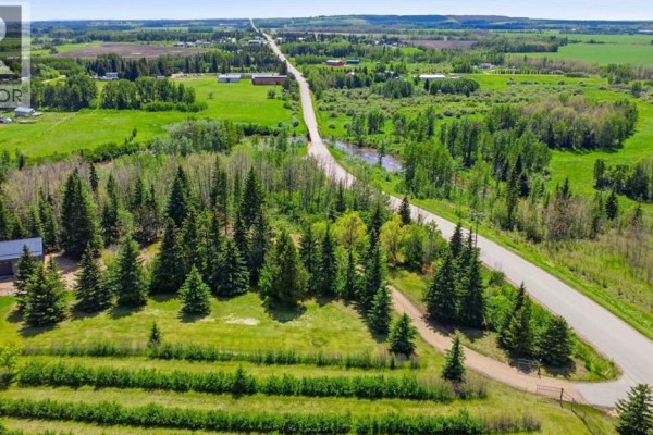 View down Range Road 30 showing surrounding green fields, trees, and distant buildings. - 440029 Range Road 30, Rural Ponoka County