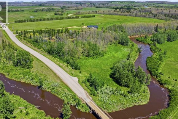 Aerial view of Range Road 30 and a meandering brown creek bordered by trees and fields. - 440029 Range Road 30, Rural Ponoka County