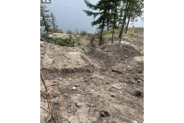 View of a sloped, undeveloped lot with trenches, dirt piles, rocks, and scattered trees overlooking a lake. - 4401 Westside Road Unit# Lot 22, Kelowna