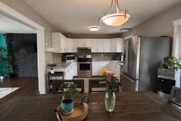 Kitchen and dining area with white cabinets, stainless steel appliances, and a wooden dining table. - 4404 54a Avenue, High Prairie
