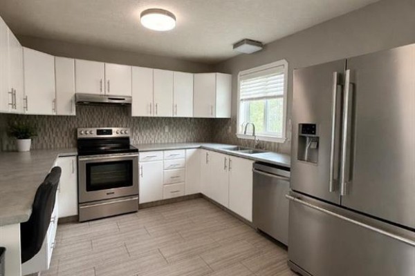 L-shaped kitchen with white cabinets, stainless steel appliances, grey tile floors, and a window. - 4404 54a Avenue, High Prairie