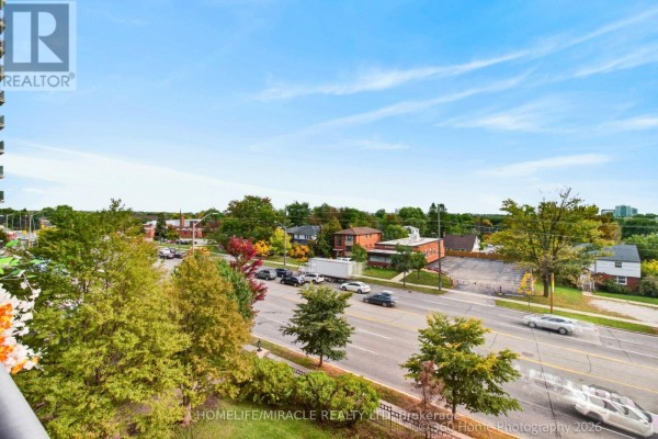 View from a balcony overlooking a suburban street with trees, houses, and moderate car traffic. - 441 - 18 Mondeo Drive, Toronto