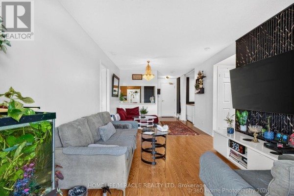 Living room with a grey sectional sofa, hardwood floors, a television on a white media console, and an aquarium. - 441 - 18 Mondeo Drive, Toronto