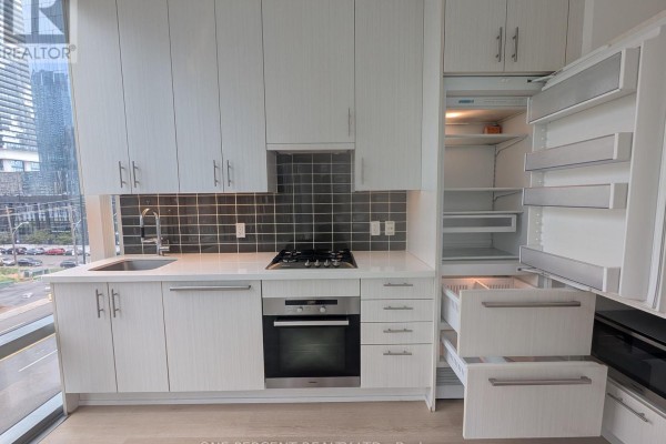 Modern kitchen with white cabinets, stainless steel appliances, black tile backsplash, and city view. - 441 - 39 Queens Quay E, Toronto