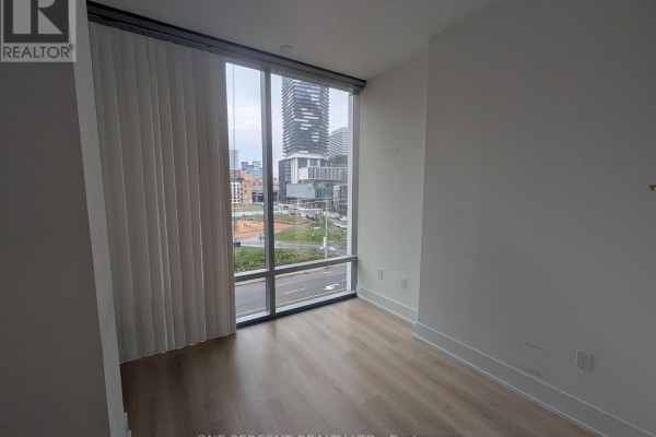 Corner of an empty room with light wood floors and floor-to-ceiling windows overlooking city buildings. - 441 - 39 Queens Quay E, Toronto